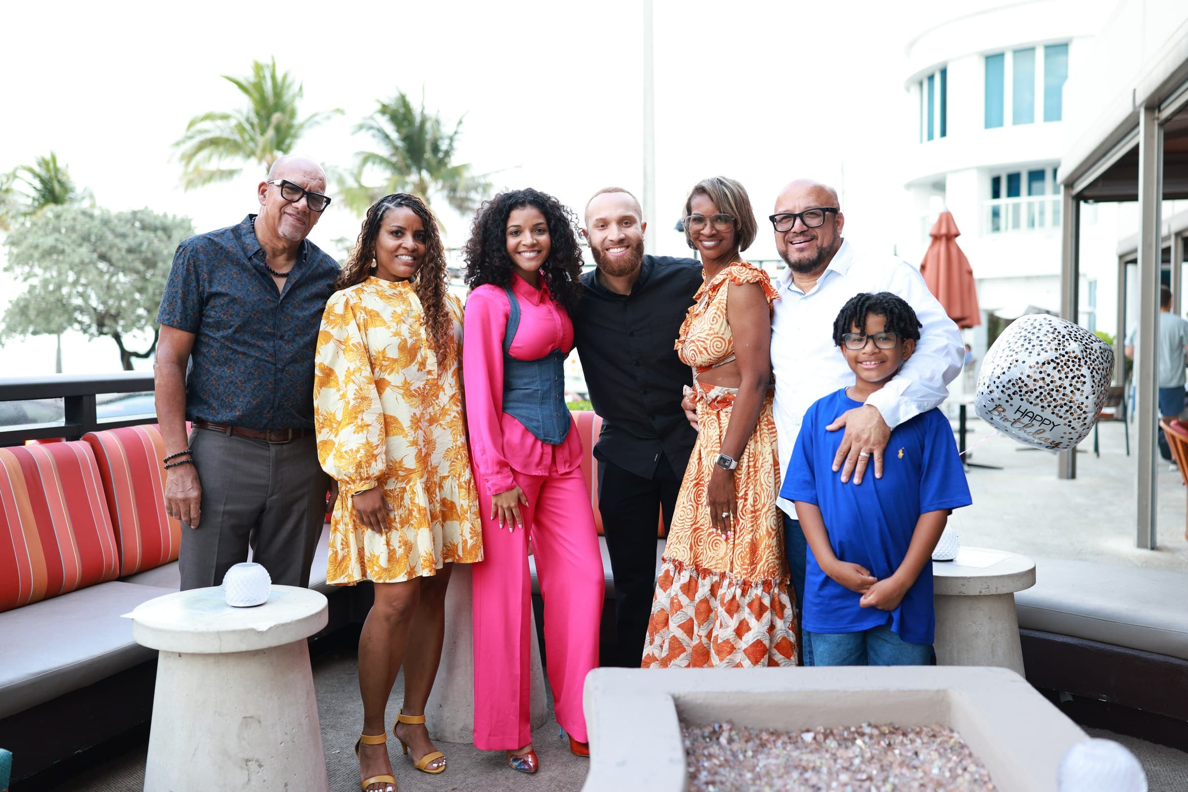 Ray and Alexia with family at a seaside birthday celebration, palm trees behind them