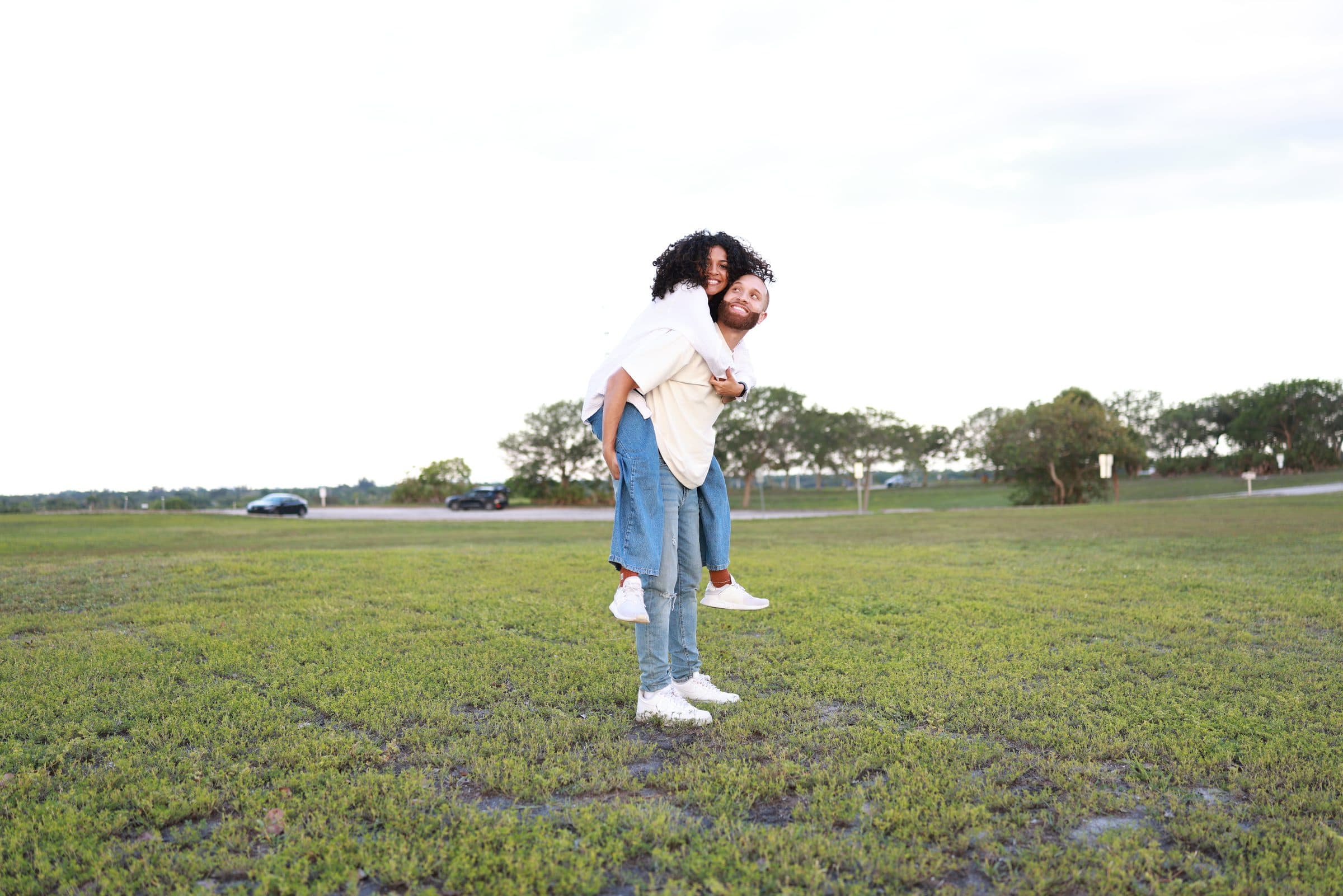 Alexia riding piggyback on Ray as they laugh together in the field