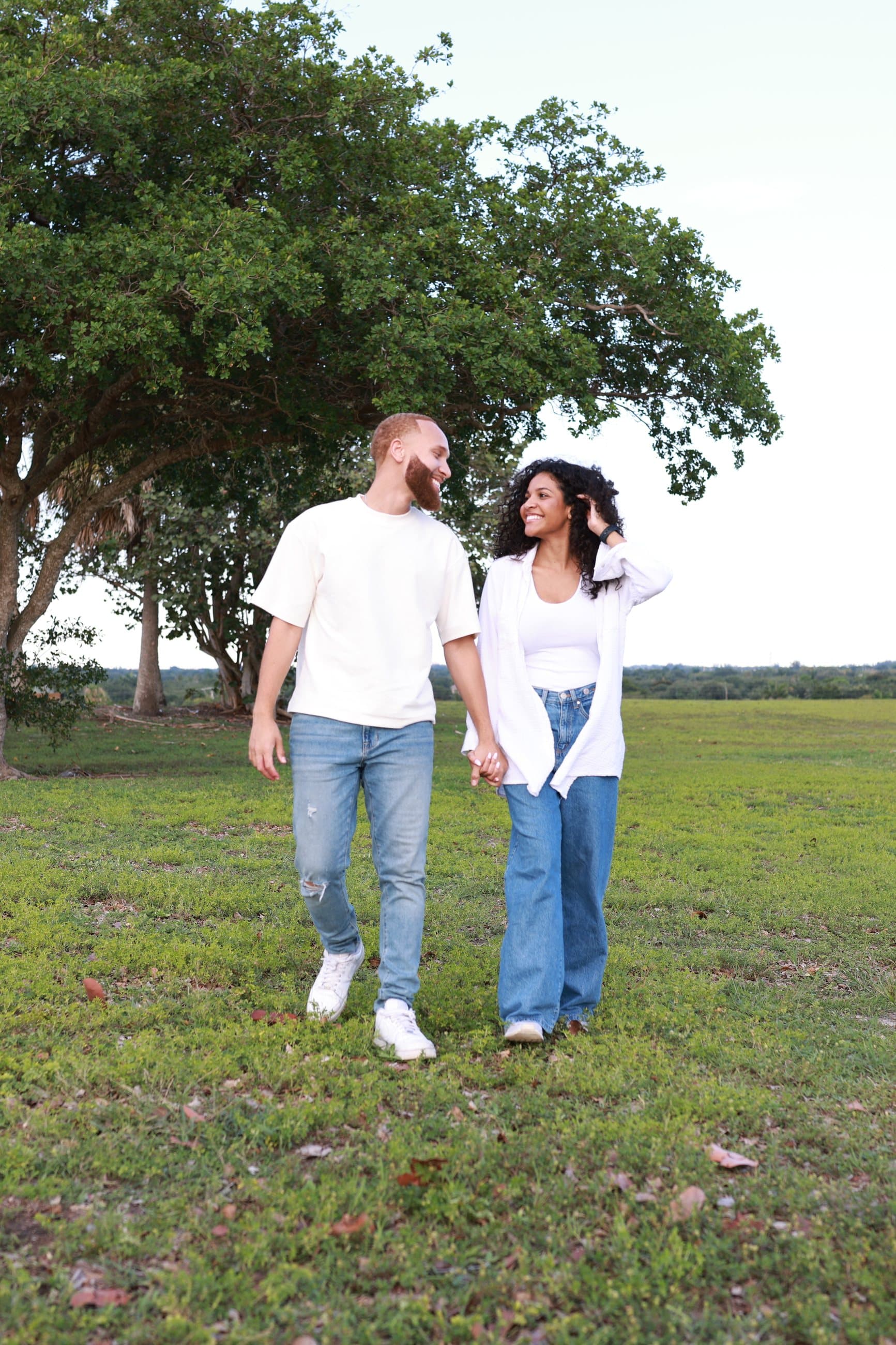 Ray and Alexia walking hand in hand beneath a large tree in a South Florida park
