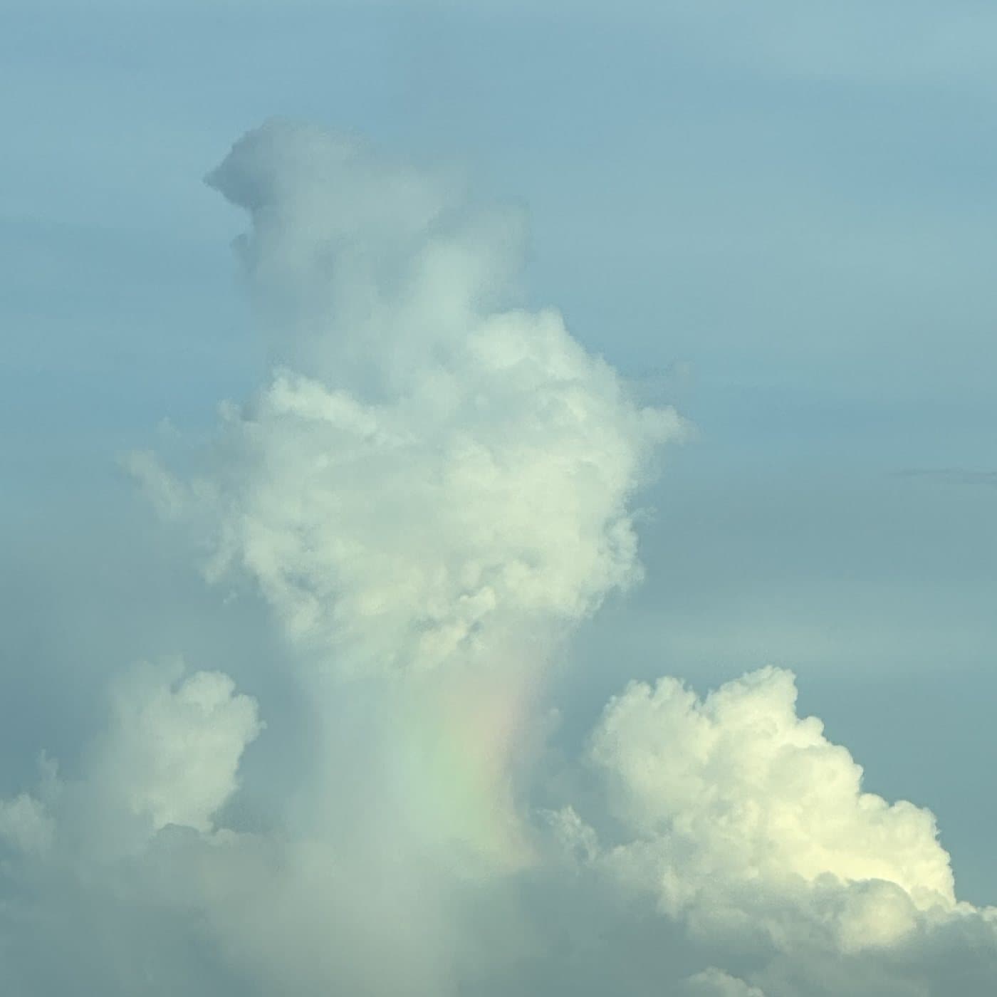 A faint vertical rainbow appearing within sunlit clouds.